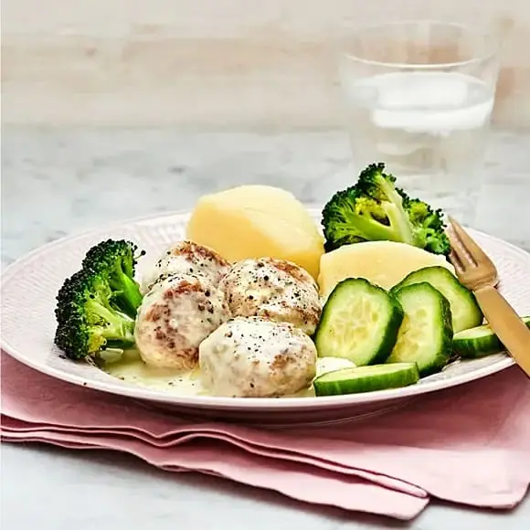 Tallrik med kycklingköttbullar i krämig sås, kokt potatis, broccoli och gurka.