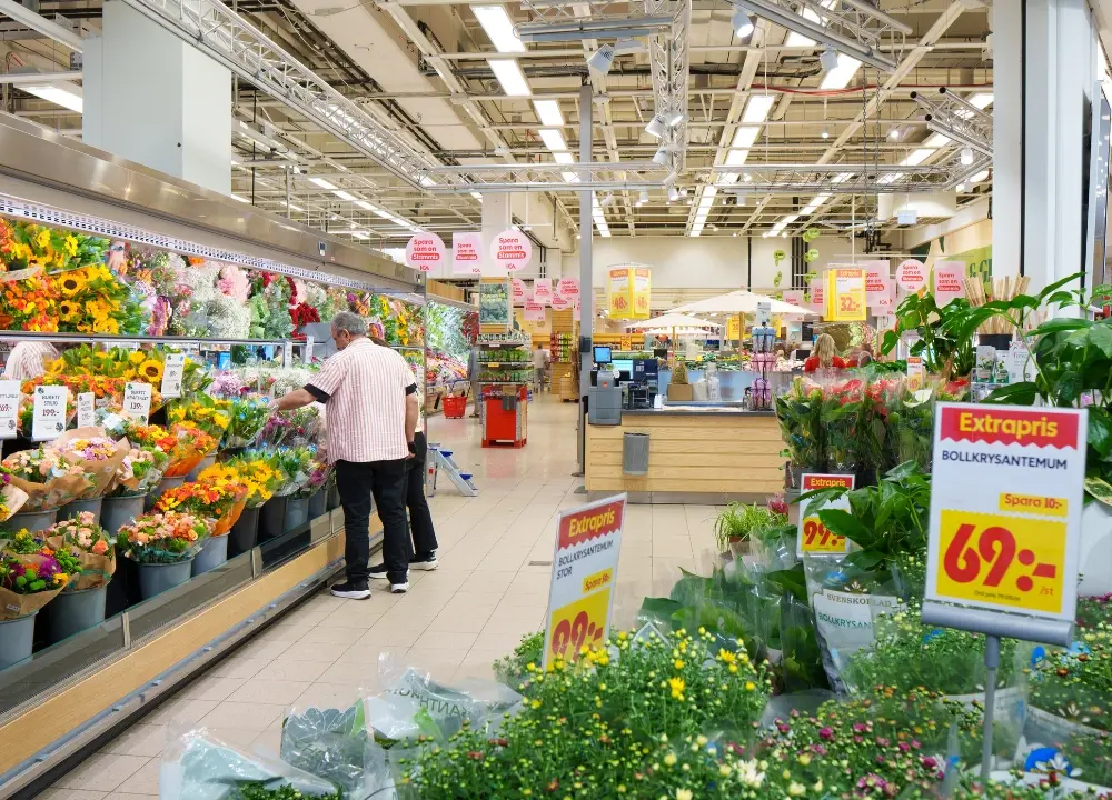 Kund tittar på blomsterbuketter i blomsteravdelningen på ICA Kvantum Gränby. Gröna växter och krukblommor syns i förgrunden.
