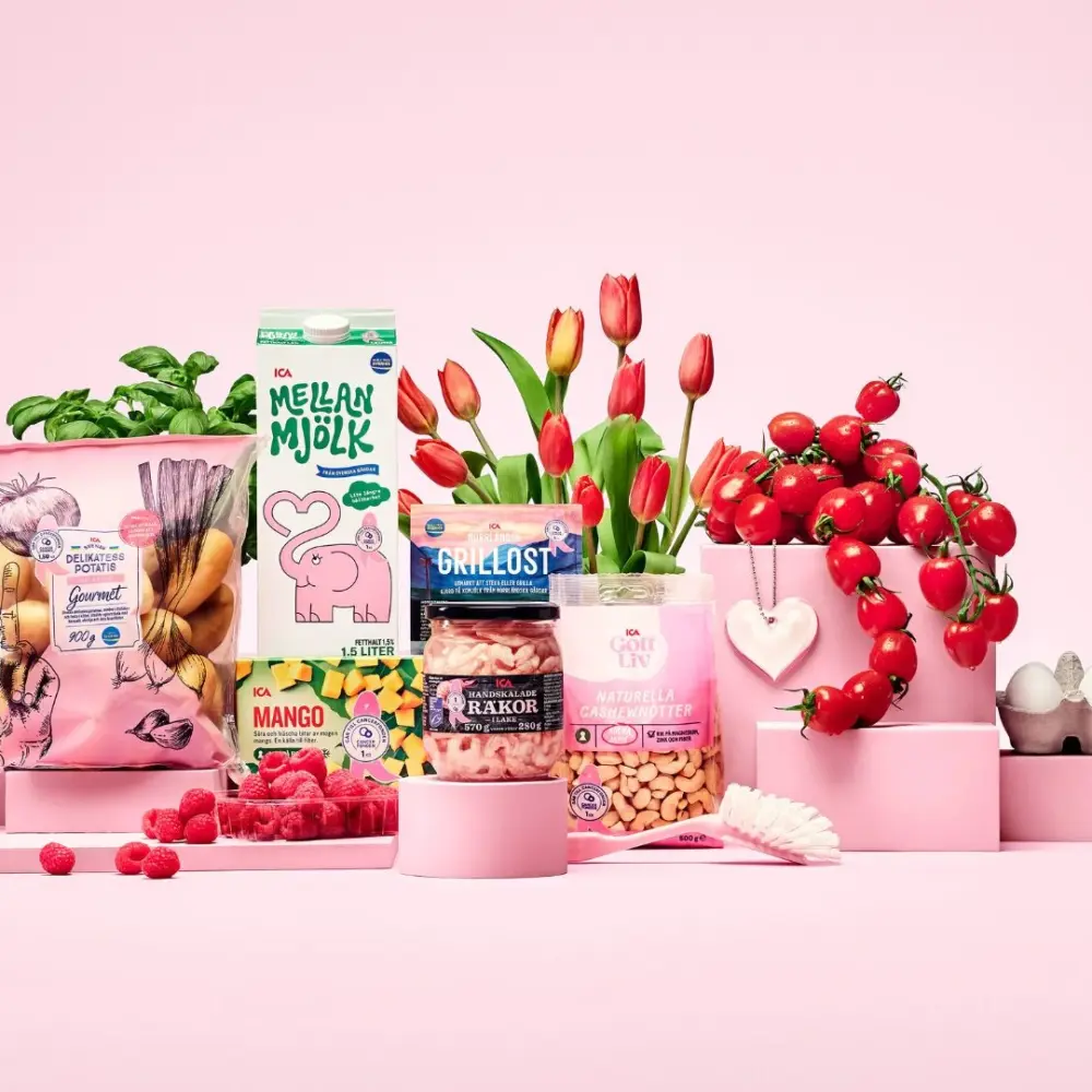 Rosa Bandet-produkter från ICA på rosa bakgrund, bland annat hallon, tomater, avokado, bröd, ägg och andra matvaror som stödjer Cancerfondens Rosa Bandet-kampanj.
